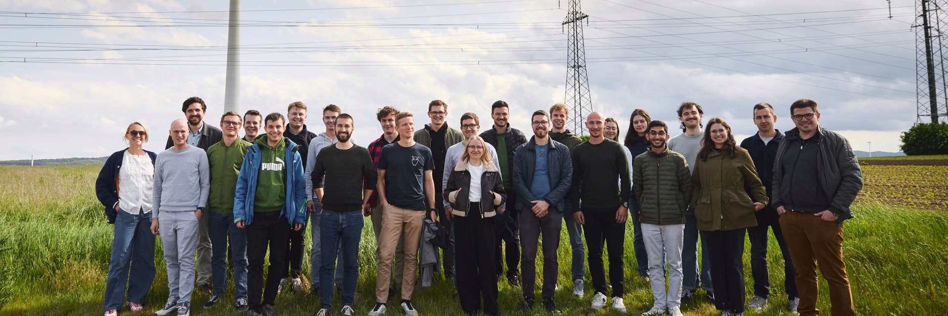 Gruppe von Menschen steht im Freien neben einem Windrad und Strommasten.