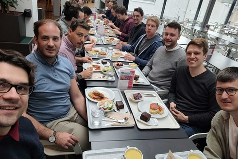 Eine Gruppe von Männern sitzt zusammen beim Essen in einem modernen Raum.