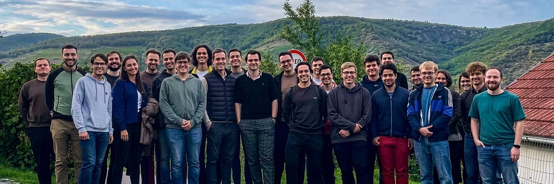 Eine große Gruppe von Menschen steht im Freien vor einer hügeligen Landschaft.