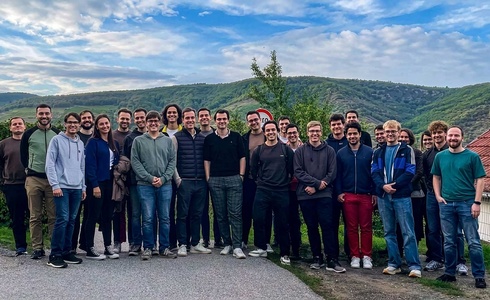 Eine große Gruppe von Menschen steht im Freien vor einer hügeligen Landschaft.