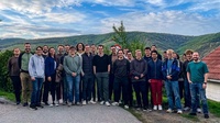 Eine große Gruppe von Menschen steht im Freien vor einer hügeligen Landschaft.