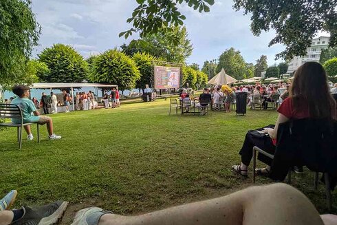 Menschen genießen eine Veranstaltung im Freien auf einer Wiese mit Leinwand.