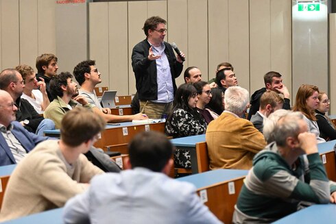 Ein Mann stellt eine Frage während einer Diskussion in einem vollbesetzten Saal.