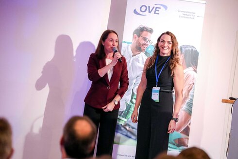 Zwei Frauen sprechen auf einer Veranstaltung vor einem Banner.