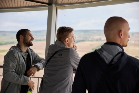 Drei Männer stehen an einem Aussichtspunkt und schauen auf die Landschaft.