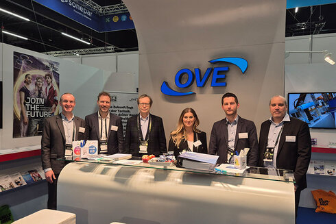 Sechs Personen stehen an einem Messestand mit dem Logo "OVE".