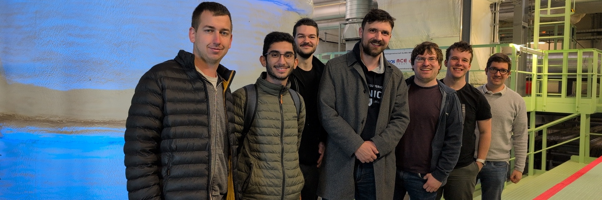 Eine Gruppe von sieben Personen steht in einer industriellen Umgebung.