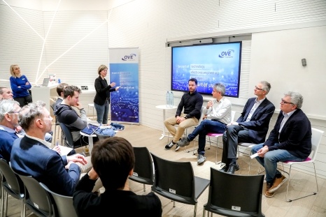 Podiumsdiskussion mit mehreren Sprechern vor einem Publikum in einem modernen Raum.
