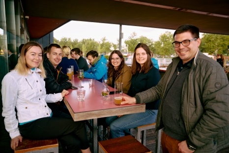 Sechs Freunde sitzen an einem Tisch und genießen Getränke im Freien.