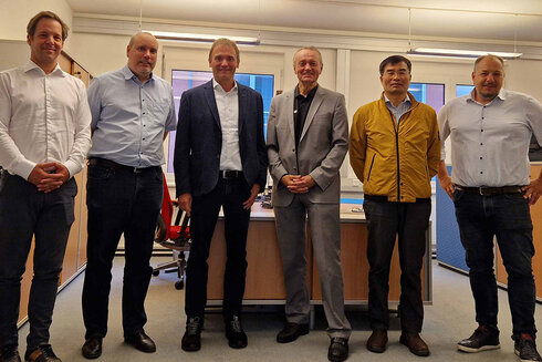 Sechs Männer in formeller Kleidung stehen nebeneinander in einem Büro.