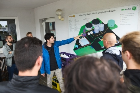 Eine Person erklärt eine Biogasanlage anhand einer Grafik an der Wand.