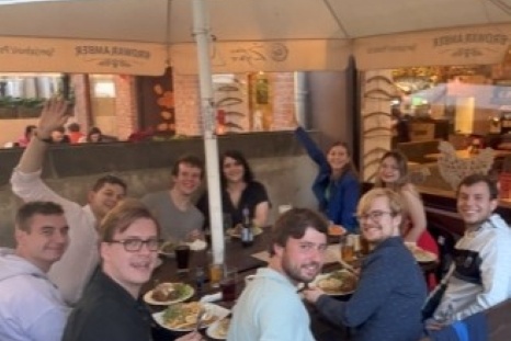Eine Gruppe von neun Personen sitzt an einem Tisch und genießt eine Mahlzeit im Freien.