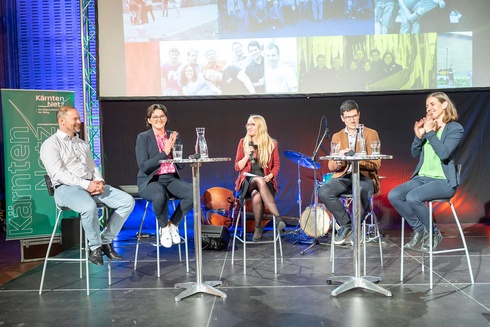 Podiumsdiskussion mit fünf Personen, die an Stehtischen sitzen und miteinander sprechen.