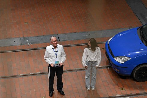 Ein Mann spricht mit einer Frau neben einem blauen Auto in einer Halle.