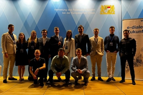 Gruppenfoto von 12 Personen in formeller Kleidung vor einer blauen Wand.