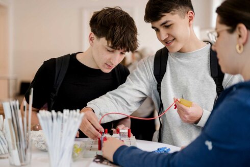 Zwei Jugendliche experimentieren gemeinsam mit elektrischen Bauteilen an einem Tisch.