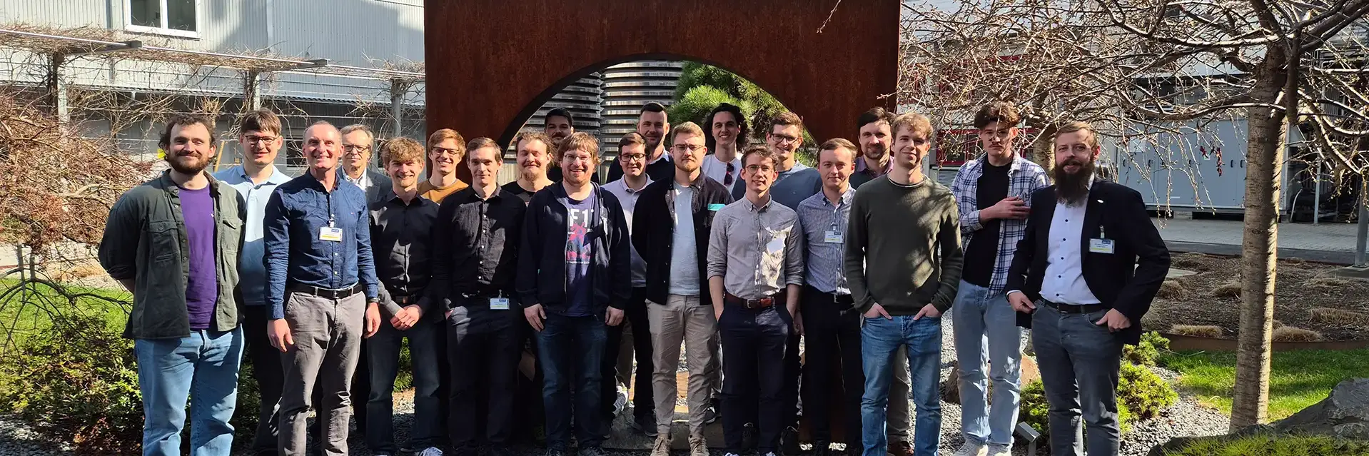 Gruppe von Männern posiert vor einem Metallbogen in einem Garten.