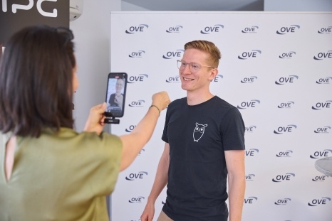 Eine Person macht ein Foto von einem lächelnden Mann vor einem Banner.