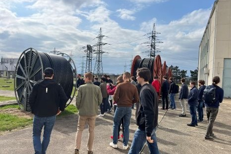 Gruppe von Menschen besichtigt große Kabeltrommeln im Freien.