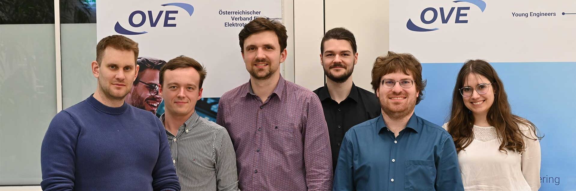 Sechs Personen stehen zusammen vor einem OVE-Plakat.