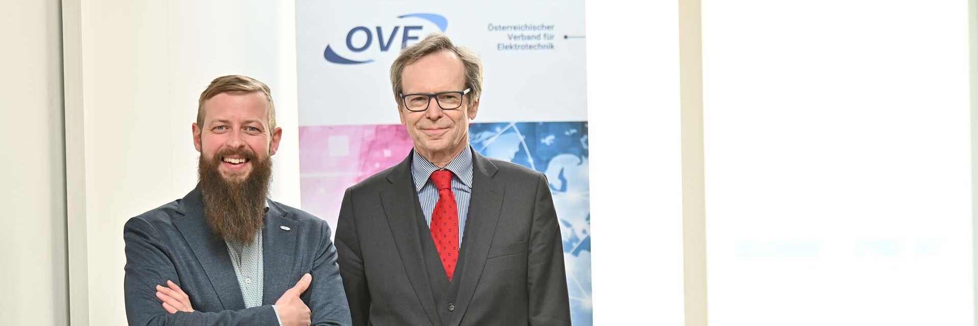 Zwei Männer stehen lächelnd vor einem OVF-Poster in einem Büroraum.