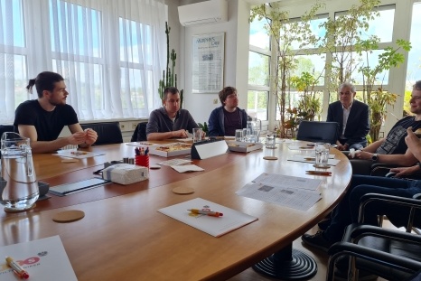 Eine Gruppe von sechs Personen sitzt an einem Konferenztisch in einem hellen Raum.