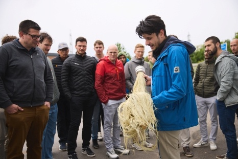 Mann in blauer Jacke zeigt Gruppe von Männern ein Werkzeug.