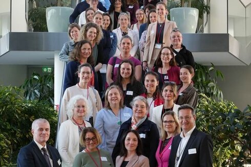 Gruppenfoto von Frauen und Männern, die auf einer Treppe in einem modernen Gebäude stehen.