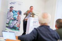 Ein Mann spricht an einem Podium vor Publikum auf einer Veranstaltung.