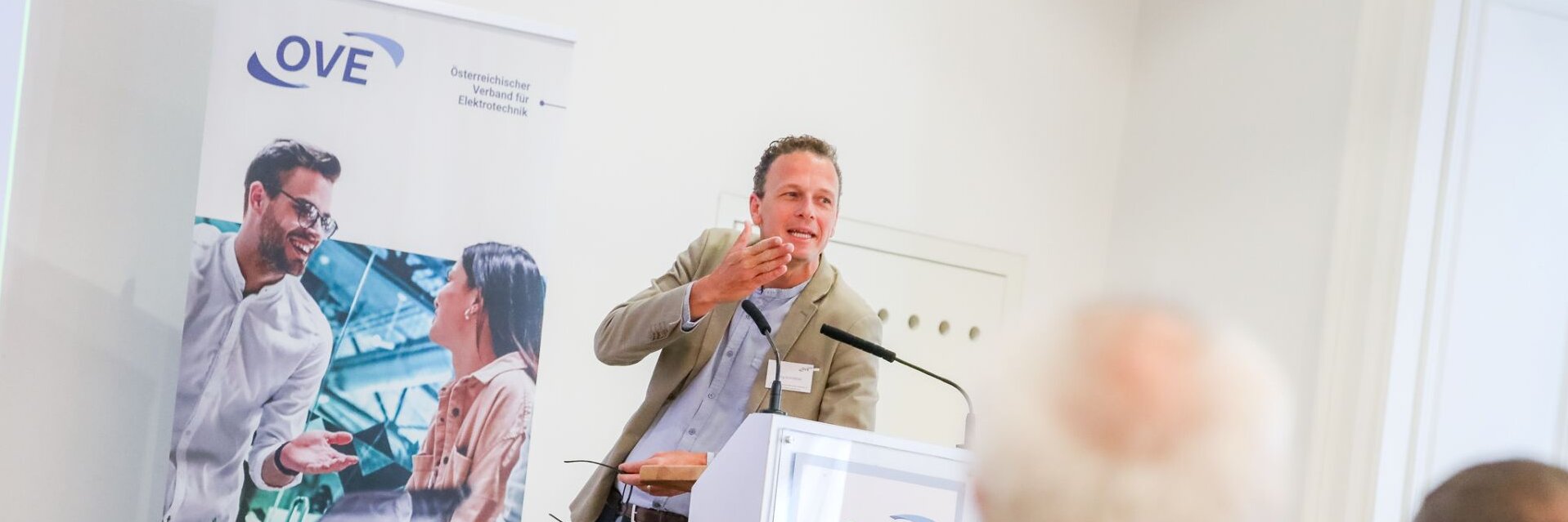 Ein Mann spricht an einem Podium vor Publikum auf einer Veranstaltung.