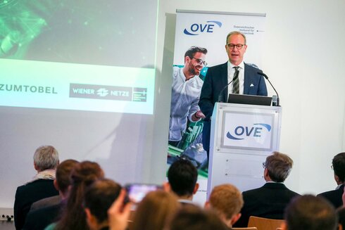 Ein Mann spricht am Rednerpult vor einem Publikum bei einer Veranstaltung.