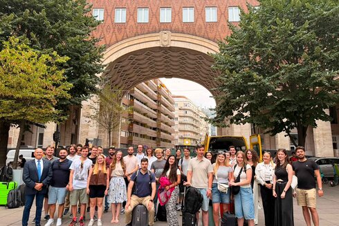 Gruppe von Menschen steht unter einem großen Bogen in einer Stadt.