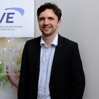 Mann in Anzug lächelt vor einem Banner des OVE.