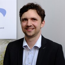 Mann in Anzug lächelt vor einem Banner des OVE.