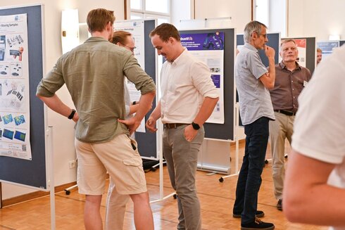 Menschen diskutieren an Stellwänden mit Präsentationen in einem Veranstaltungsraum.