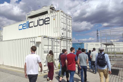 Gruppe von Personen geht an Containern mit der Aufschrift "cellcube" vorbei.