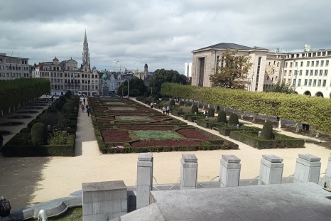 Garten mit geometrischen Beeten und Bäumen, umgeben von Gebäuden in einer Stadt.