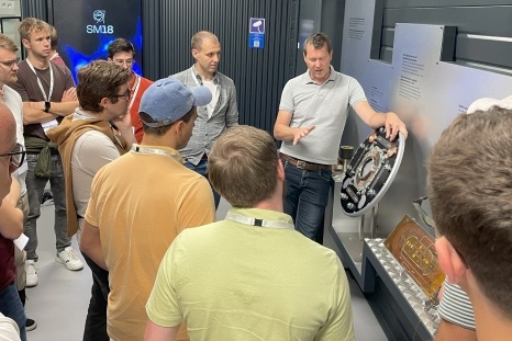 Eine Gruppe von Personen hört einem Dozenten zu, der eine technische Komponente erklärt.