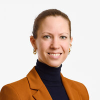 Frau mit kurzen Haaren in einer orangefarbenen Jacke lächelt freundlich in die Kamera.