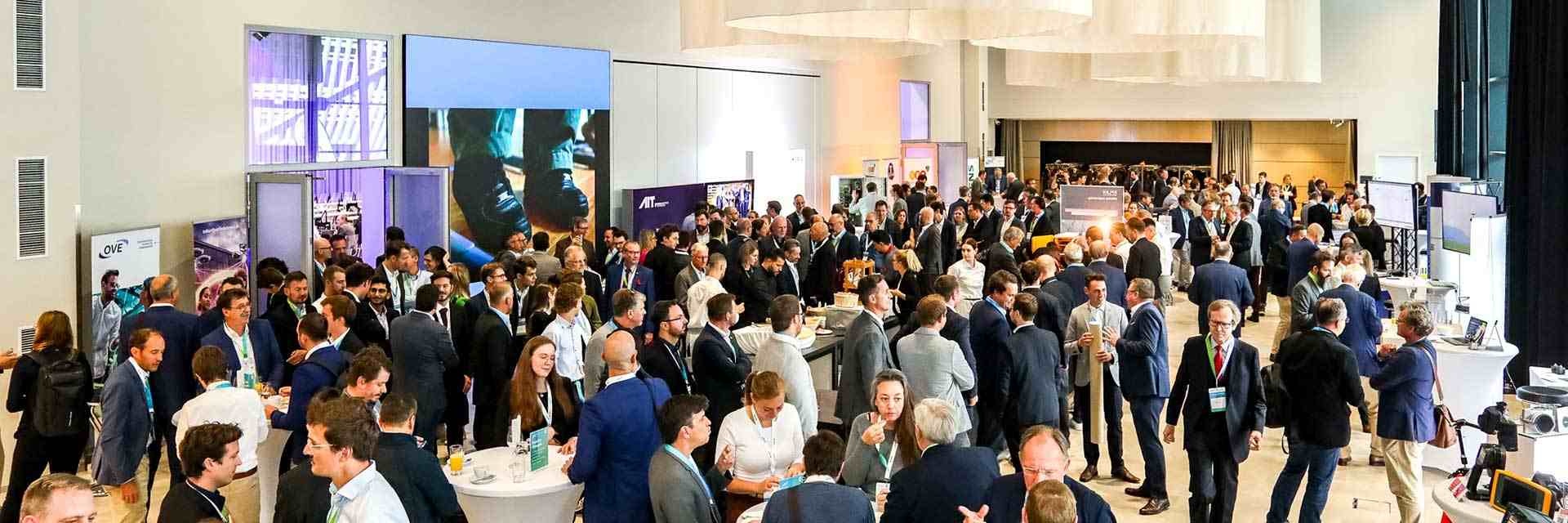 Menschenmenge auf einer Konferenz mit Stehtischen und Ausstellungsständen.