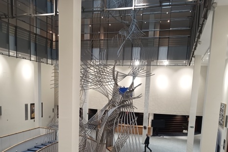Moderne Skulptur in einem hellen, offenen Raum mit Treppe und Personen.