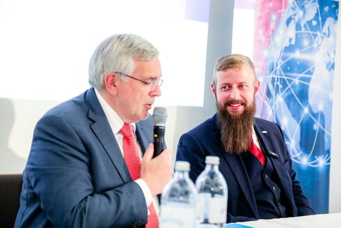 Zwei Männer am Tisch sprechen während einer Veranstaltung.
