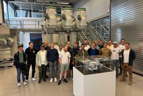 Gruppe junger Männer steht vor Maschinen in einem modernen Technikraum.