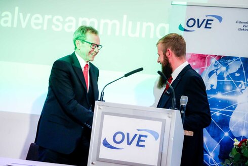 Zwei Männer schütteln sich die Hände bei einer Versammlung des OVE.