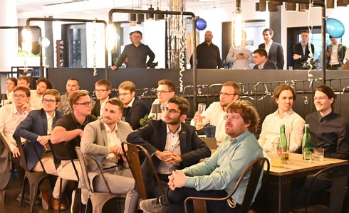 Eine Gruppe von Menschen sitzt aufmerksam in einem modernen Veranstaltungsraum.