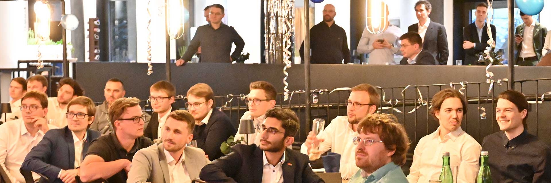 Eine Gruppe von Menschen sitzt aufmerksam in einem modernen Veranstaltungsraum.