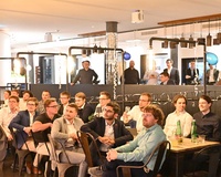 Eine Gruppe von Menschen sitzt aufmerksam in einem modernen Veranstaltungsraum.