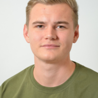 Ein junger Mann mit blonden Haaren und einem grünen T-Shirt schaut in die Kamera.