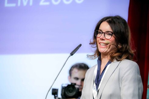 Frau am Rednerpult lächelt während einer Präsentation.