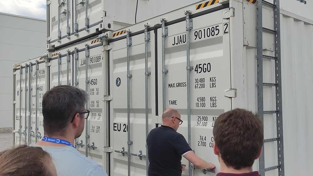 Besucher betrachten einen großen Container mit der Aufschrift "Cellcube".